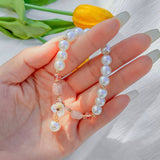 Hand holding imitation pearl chain bracelet with gold accents and decorative charm on white background with yellow flower