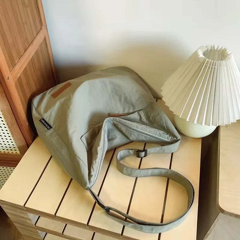 Minimalist Japanese style unisex shoulder bag in beige on wooden table next to white pleated lamp