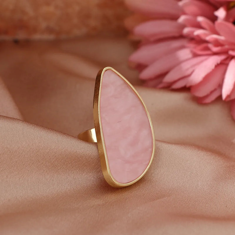 Fashion woman ring with pink stone and gold setting on satin fabric near pink flower