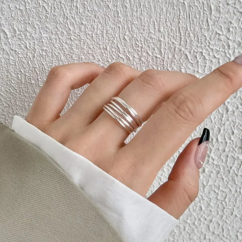 Hand wearing silver Fidget Spinner Rings on fingers against textured white wall background