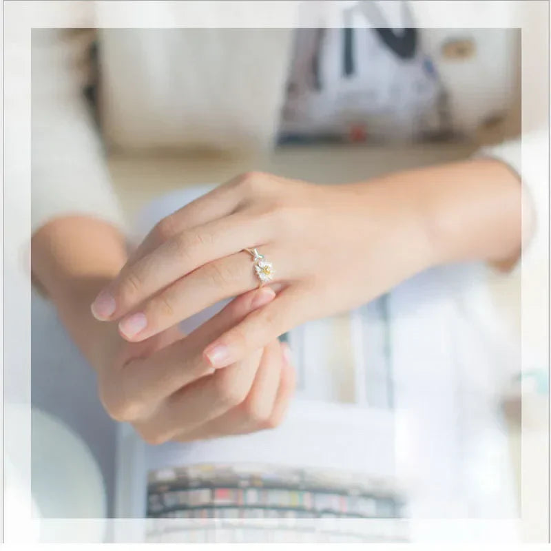 Close-up of a hand wearing a pink romantic flower ring with zircon petals on a blurred background