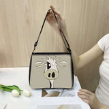 Cow print small shoulder bag with cartoon cow face design held by a woman