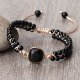 Black onyx natural stone beads bracelet with adjustable beige cord and gold-tone centerpiece on wooden surface