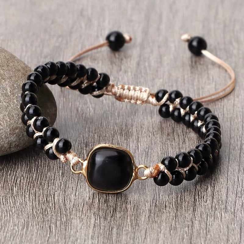 Black onyx natural stone beads bracelet with adjustable beige cord and gold-tone centerpiece on wooden surface