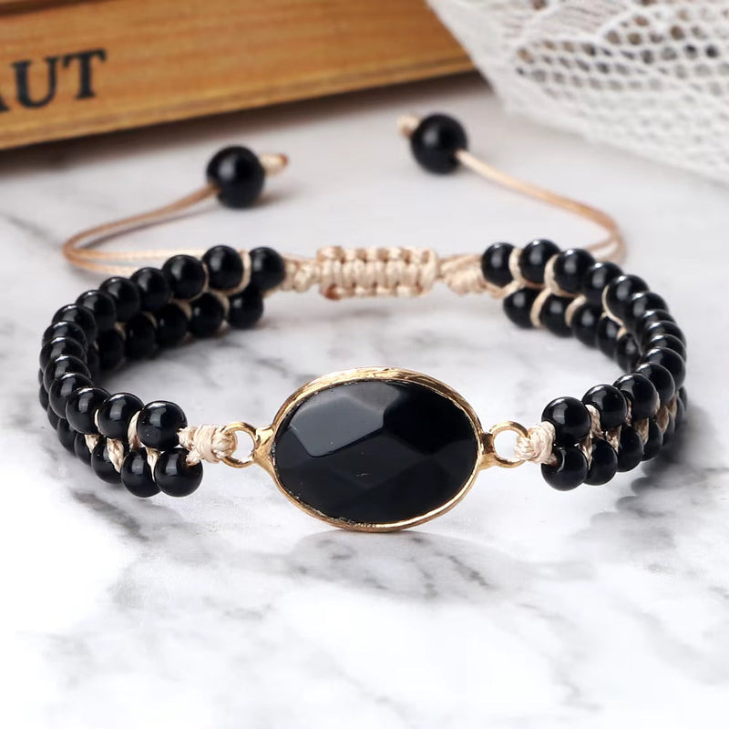 Adjustable natural stone beads bracelet with shiny black onyx and gold accent on marble background