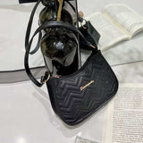 Black quilted shoulder bag with gold logo on white surface near open book